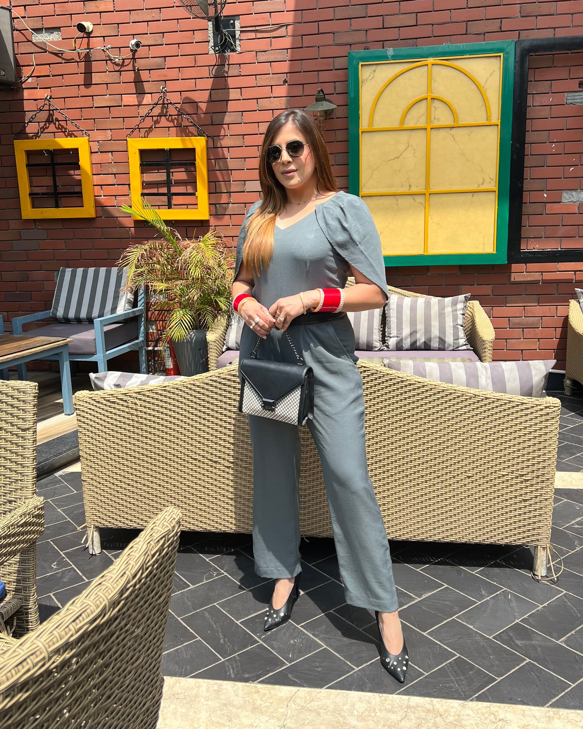 A person wearing a grey jumpsuit with sleeve detailing, standing in a outdoor seating area.