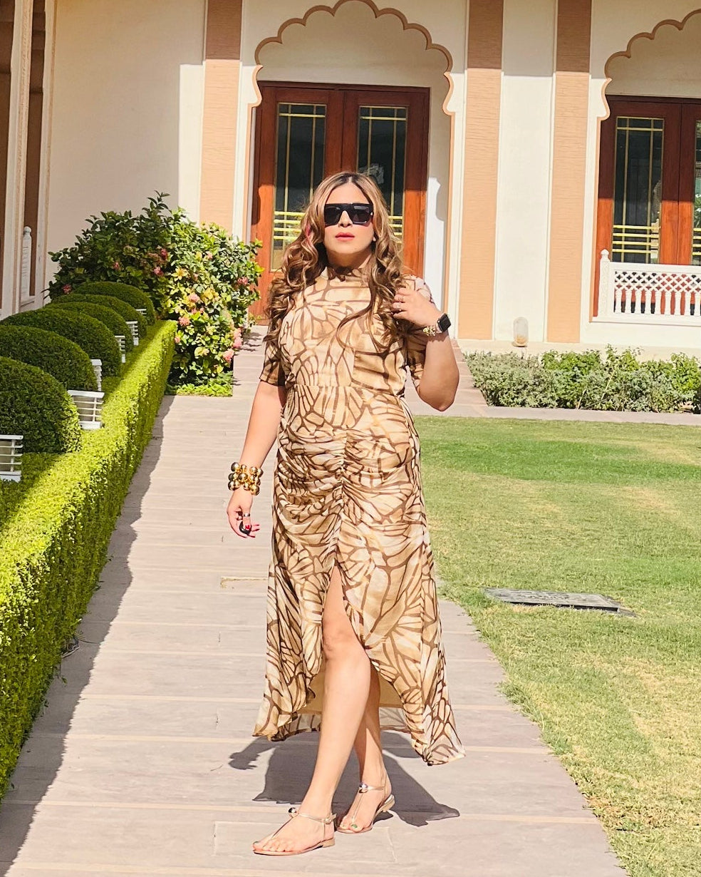 A person wearing a beige floral drape midi dress with a full collar and a tie knot at the back neck style, standing in a garden.