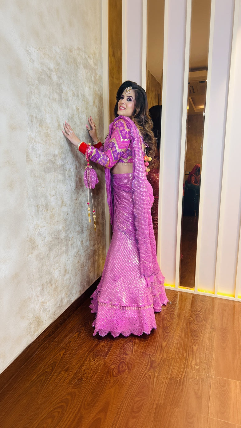 A woman posing in a lilac sequin saree with full sleeves and a V-neck backless design, featuring sequin work on pure georgette fabric.