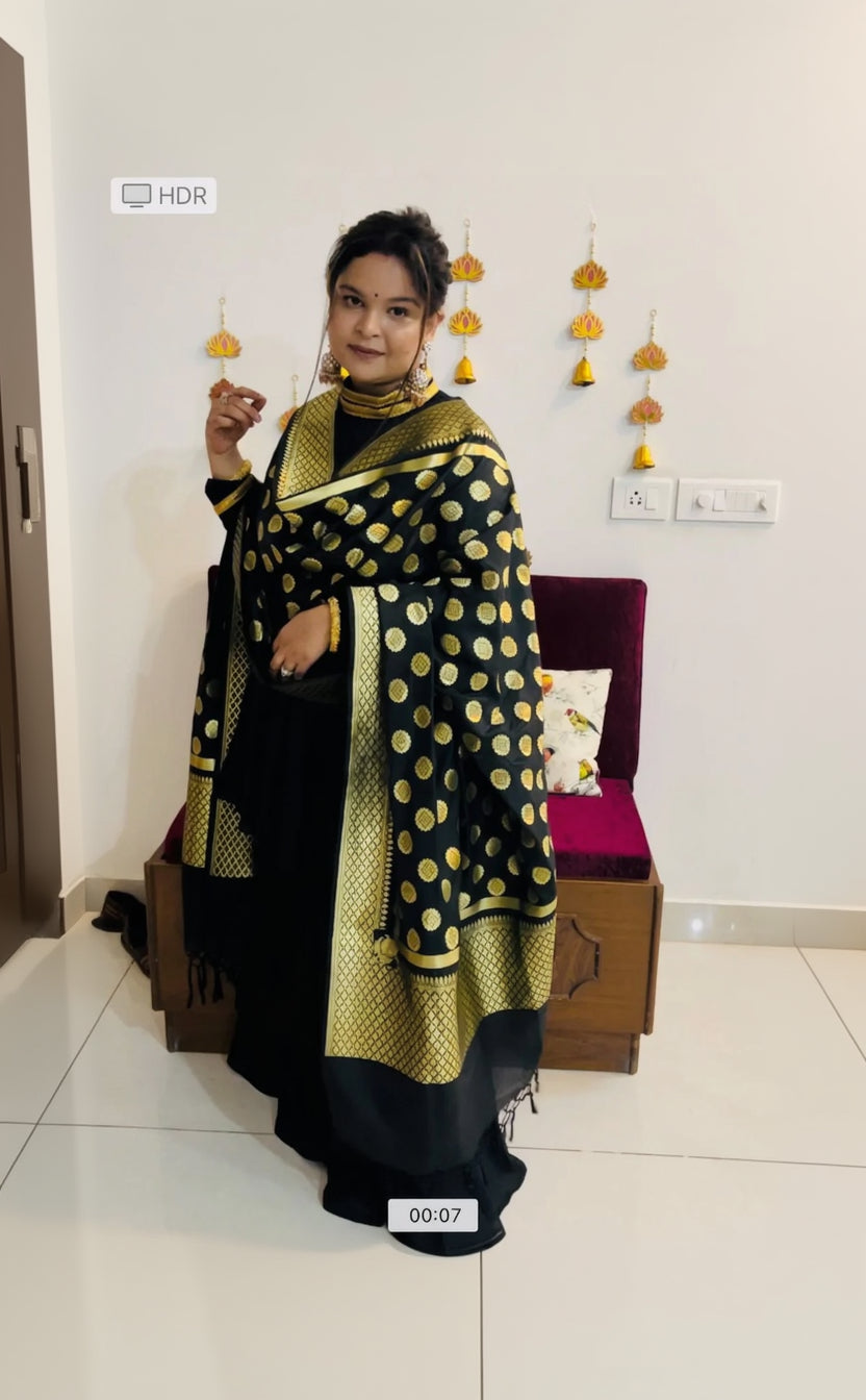 A woman wearing a traditional black and gold Garara suit with a dotted pattern on the dupatta, posing against a festive background.